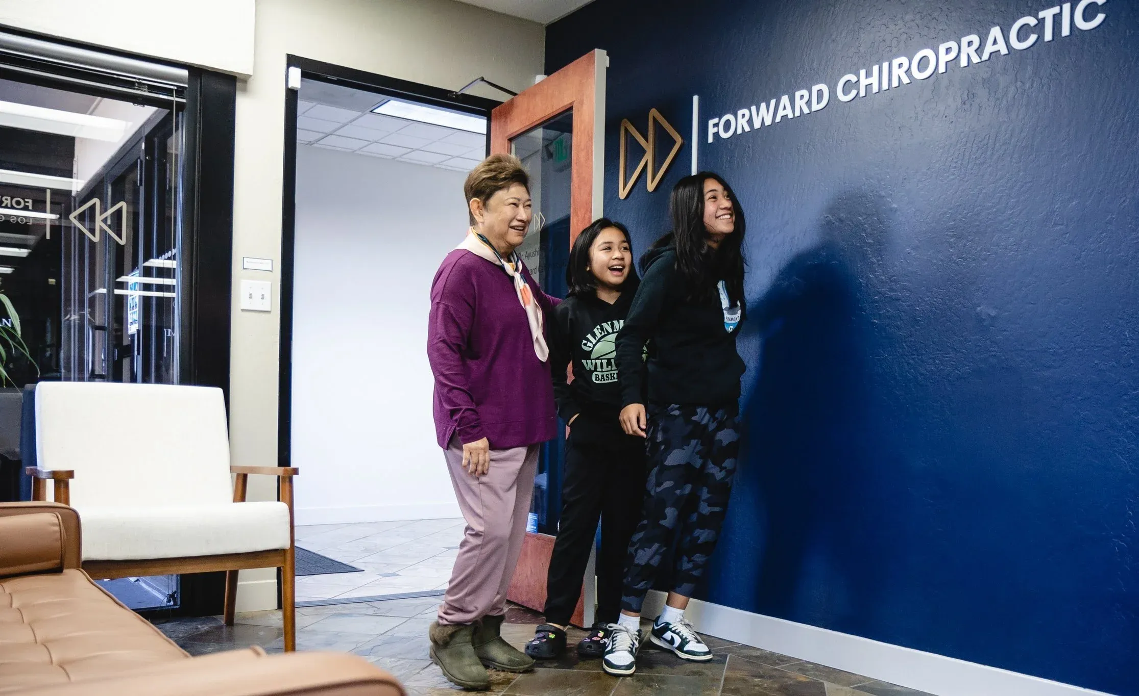 Patients laughing by the Forward Chiropractic logo wall in the clinic lobby